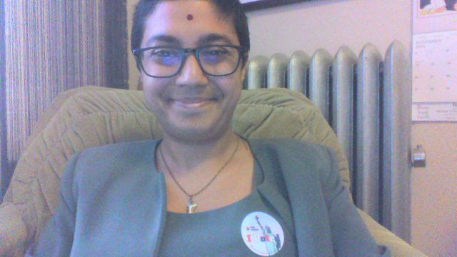 Sumana in a chair, smiling, wearing an 'I Voted' sticker