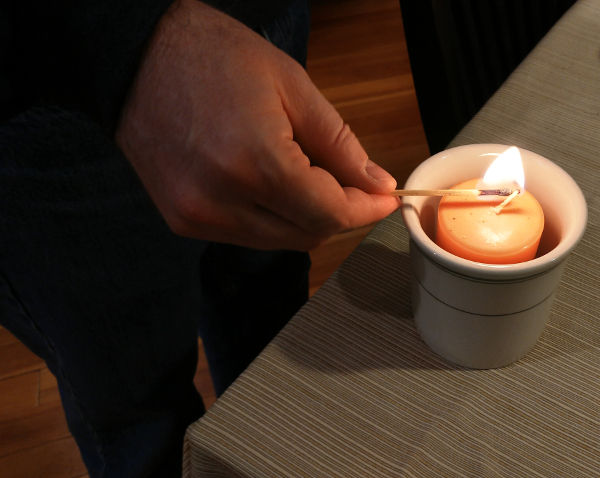 Close-up of a hand lighting an orange candle.