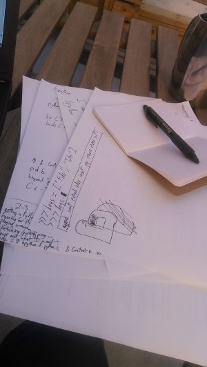 half-scratched-out bpython logo, Python code, and technical prose written and drawn on paper, with notebook and pen, on a wooden table that also has a mug and a laptop on it
